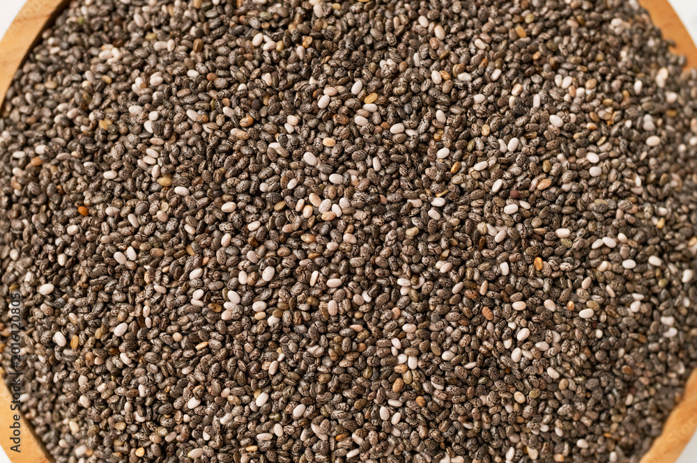 Fototapeta premium Close-up of dry chia seeds in wooden bowl, top view. Food background, healthy seeds for breakfast, snacks, chia pudding. Superfood, texture of Salvia hispanica seeds 