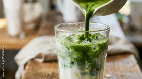 Fotografie Vibrant green matcha is gracefully poured into a chilled glass of creamy milk and ice, creating a beautiful marbled swirl on a rustic wooden table