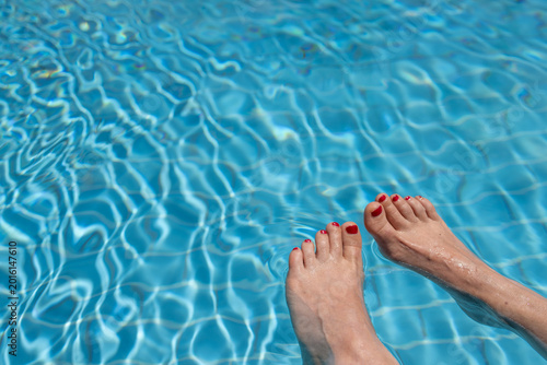 Fotografie Woman relaxing in clear blue swimming pool water with red painted toenails and s
