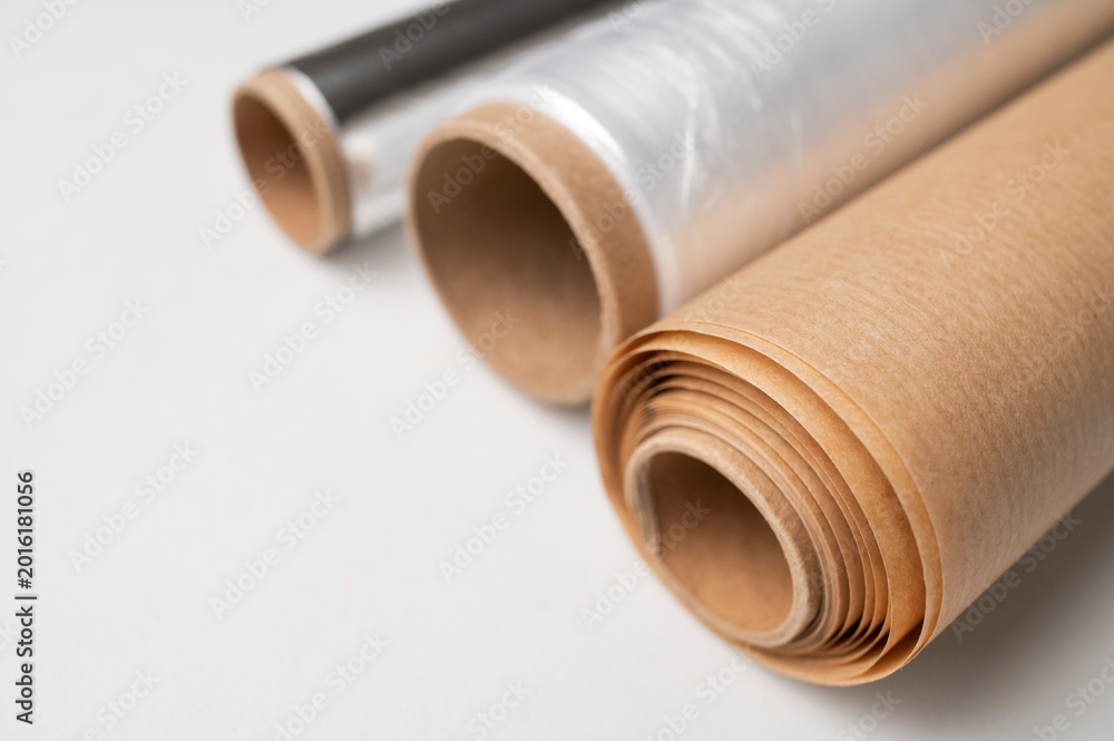 Fototapeta premium Three rolls of kitchen packaging materials on gray background, flat lay top view. Plastic cling film, aluminum foil, baking paper (parchment)