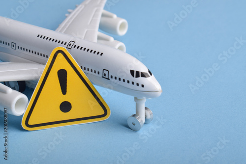 Fotografie Toy airplane beside a yellow warning sign on blue background representing aviation safety, flight risk, travel alerts, air transport issues, turbulence, delays, and airline warning concept