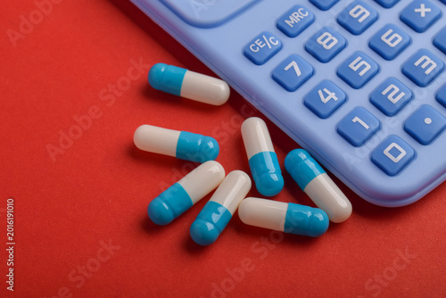 Medicine capsules and calculator on red background representing healthcare expenses, pharmacy costs, medical budgeting, insurance payments, and treatment finance concept.