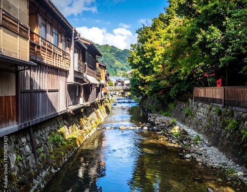 Traditional Japanese Wooden Buildings Along A Scenic River Canal In A Historic Town With Lush Green Trees And Mountain Background Under Bright Blue