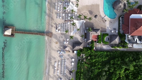 Panning view of a wooden pier with a brown roof extending into the vibrant turquoise waters contrasting with the white sandy beach,aerial shot, La Romana, dominican republic.