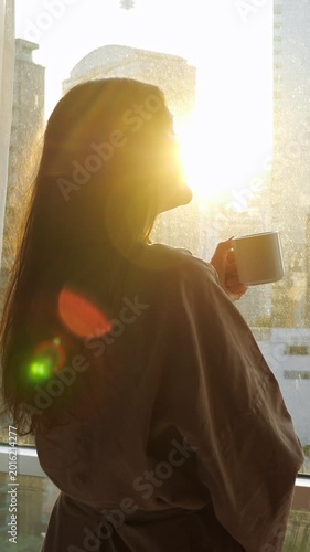 Morning Coffee Ritual. Hotel Guest Relaxes Beside Window With Morning Beverage And Cityscape. Early Morning Routine Includes Woman Savoring Coffee While Observing Bustling City From Hotel Window
