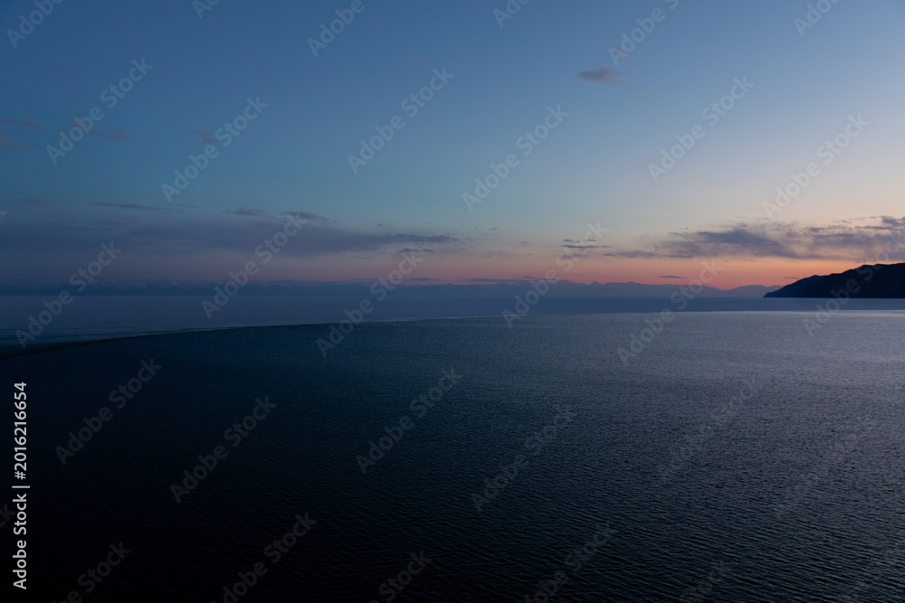Fototapeta premium Wide twilight landscape of the Angara River flowing into Lake Baikal near Listvyanka, Irkutsk Oblast, Russia, with calm water, distant mountains and pastel sky