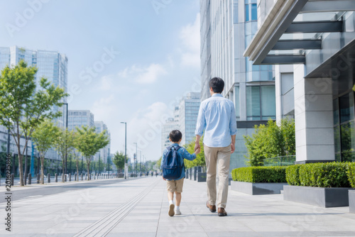 Father walking with young son in modern city street holding hands