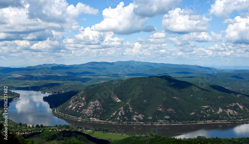 the riverbend of the Danube river at Zebegeny village, and Nagymaros, Hungary. lush green hills in the background. popular summer holiday destination. smooth calm water surface. blue sky, white clouds