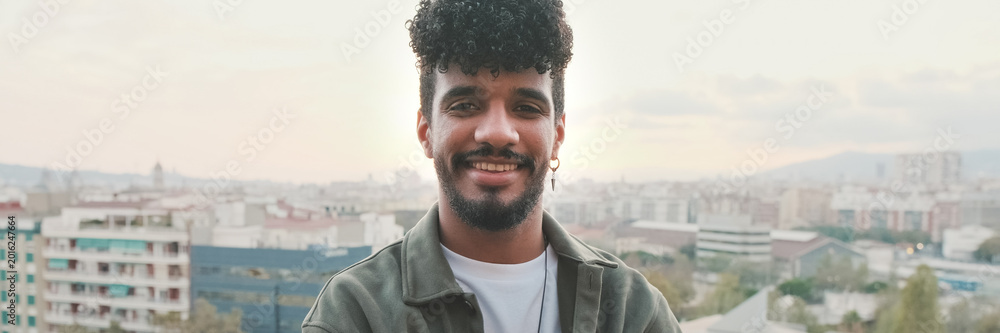Naklejka premium Close-up of smiling young guy posing at the camera while standing on the balcony. Panoramic