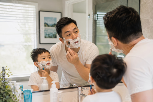 Father and son shaving together in bathroom mirror