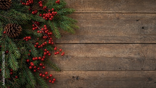 Festive evergreen branches with red berries on rustic wood.