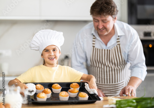 Foto Little daughter helps her father prepare cupcakes in oven at home kitchen