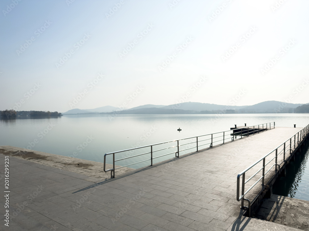 Obraz premium Tranquil Reflection: A Peaceful Lake Dock Under Misty Mountain Horizon
