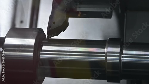 Slow motion video of a high-precision CNC lathe machine performing the finishing process on a metal shaft part.