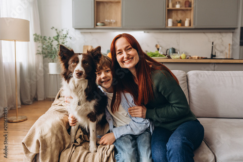 Canvastavla Woman hugs boy and dog on sofa while all smile warmly during family moment
