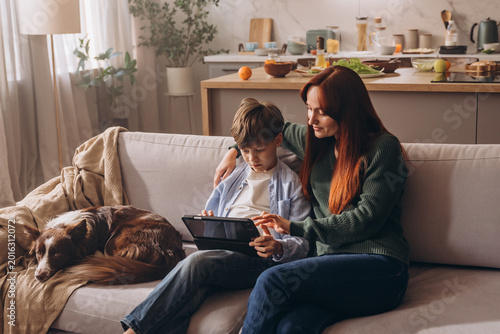 Redhead woman and boy using tablet with their dog nearby
