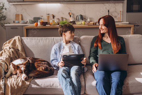 Mother and son talking and smiling while using digital devices at home
