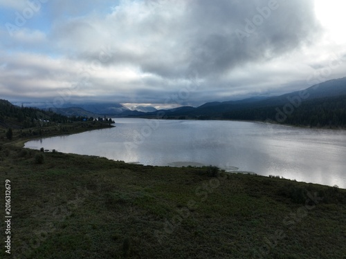 Serene lake reflecting cloudy skies with distant forested hills under soft diffused light
