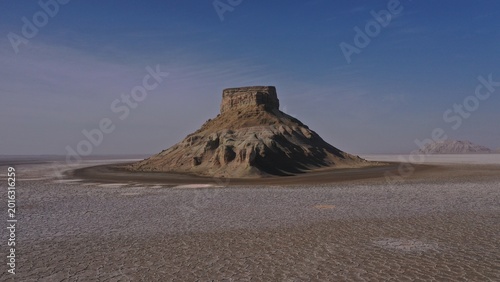 Ancient Desert Butte Rises Majestically Over Cracked Salt Flats Under Clear Blue Sky