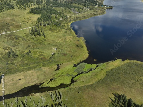 Aerial view of serene lake bordered by lush green wetlands and forested hillsides