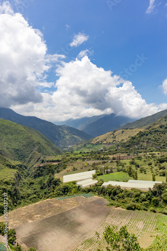 Drone aerial view of a rural farm surrounded by lush green mountains in Tenerife Valley, Colombia. Agricultural fields with neatly planted crops, countryside houses, rolling hills, and natural landsca