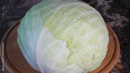 Water droplets on a head of cabbage. Water from a spray bottle lands on a head of fresh white cabbage and runs off in large droplets onto a wooden cutting board on a kitchen table. Close-up. Video 4k