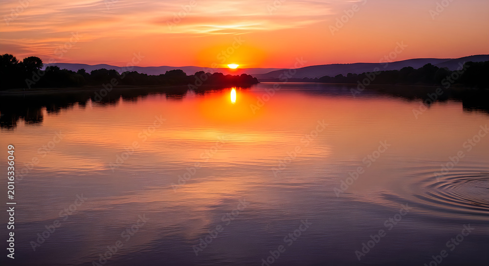 Obraz premium Dramatic sunset over calm water with city skyline silhouette