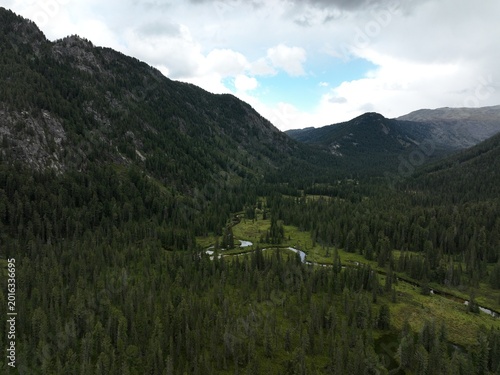 Aerial view of winding river through dense forested valley surrounded by towering mountains