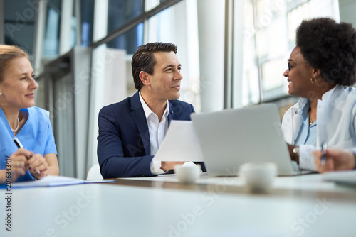 Quadro su tela Happy businessman talking to group of medical experts during a meeting in hospital