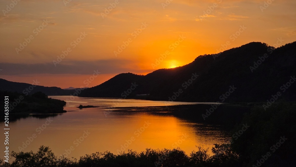Fototapeta premium Sunset River Landscape with Forested Hills and Golden Reflection