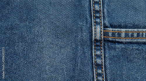 Close-up texture of blue denim fabric with visible stitching and seams, showcasing a classic casual wear material and its construction details