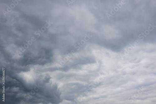 Mixed cloudscape with dark brooding storm clouds contrasting against lighter striated cloud layers across a grey sky