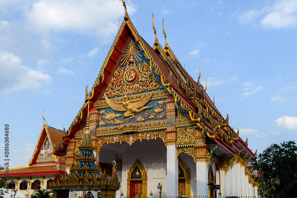 Fototapeta premium The magnificent facade of Wat Mongkol Nimit in Phuket Town. The golden pediment of this Buddhist temple features a majestic Garuda and intricate Thai motifs, framed by white pillars.