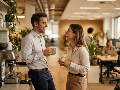 Two Coworkers Laughing Over Coffee In A Modern Open-Plan Office Kitchen During Break