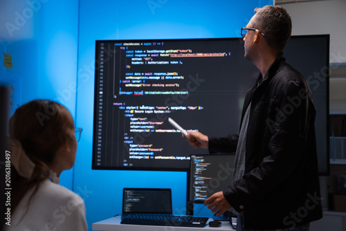 Software developers discussing code on large screen in office