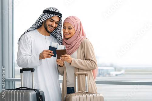 Smiling Muslim couple with luggage at airport, joyful travel moment