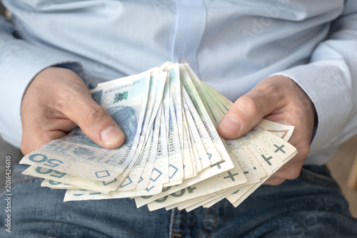 Fotografie A businessman in a light shirt holds Polish money in his hand.