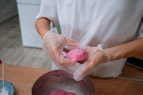 Hands wearing disposable gloves shaping a round, vibrant pink mochi dough ball on a wooden table, preparing a traditional homemade japanese sweet dessert