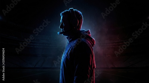 Man wearing headphones and a hooded jacket standing in a stadium with blue and red lighting