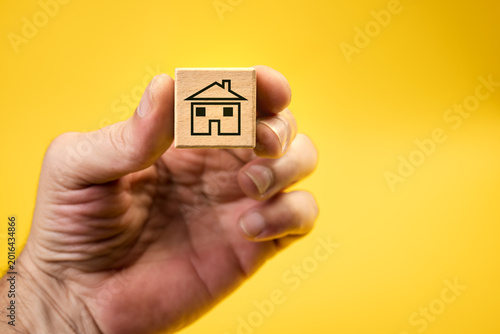 Home financing and mortgage represented by an icon of a house printed on a wooden cube held by a hand. Purchase of real estate, home, or property security. Real estate, financial, or business concepts