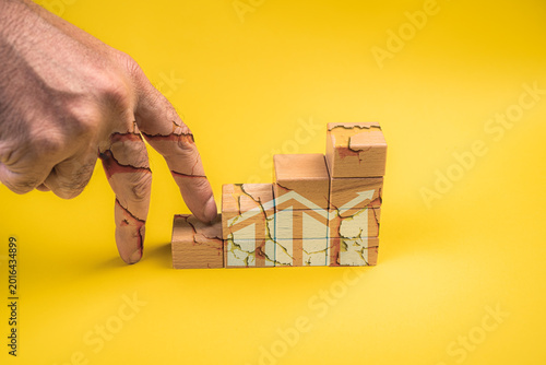 Business success and growth, path to success, fraught with difficulties, challenges, hard work, effort, and sacrifice, is represented by a broken hand climbing a wooden blocks with statistical graphic