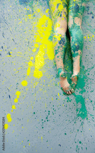 Bare legs covered in green paint resting on splattered surface with vivid yellow pigment creating an abstract artistic composition full of texture movement and creative energy