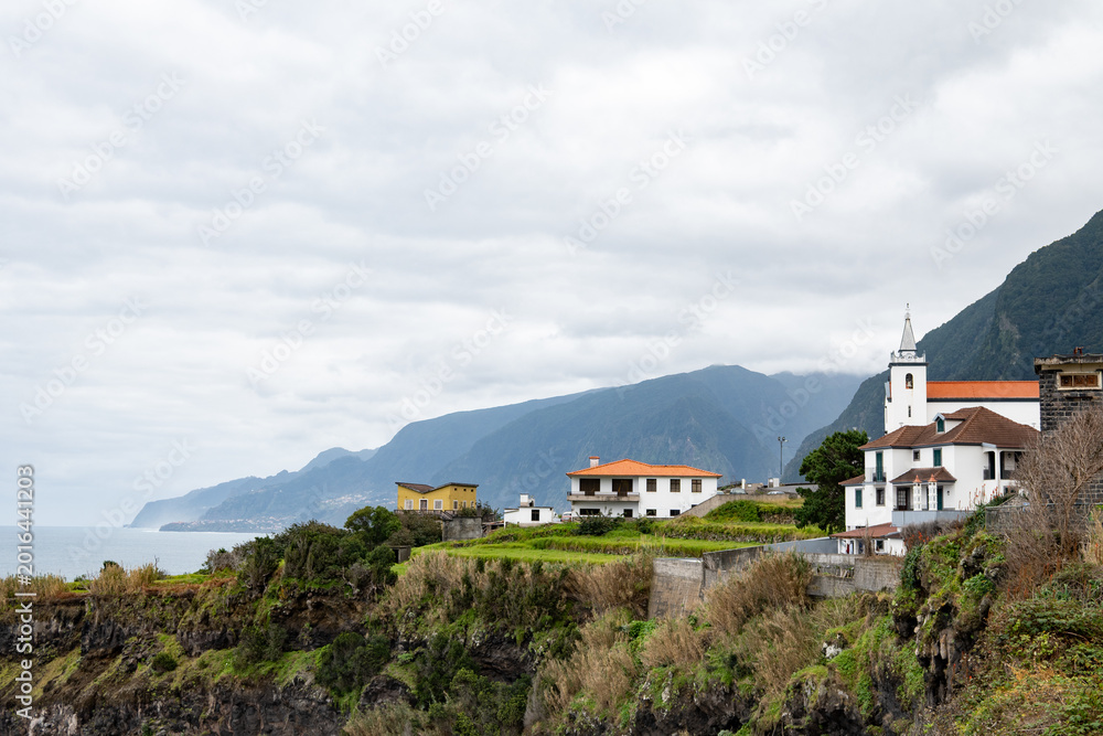 Fototapeta premium picturesque coastal village with church overlooking rocky cliffs under cloudy sky