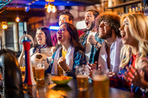 Passionate fans with white scarves cheering for soccer goal in pub.