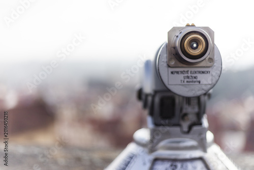 View of a tourist telescope eyepiece overlooking blurred historic rooftops and the city skyline in Prague, Prague, Czechia.
