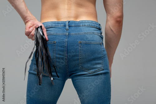 Cuadro en lienzo young athletic guy with an elastic ass is dressed in jeans and stands with his back to the camera, with a whip in the back pocket of his jeans for lovemaking with his wife