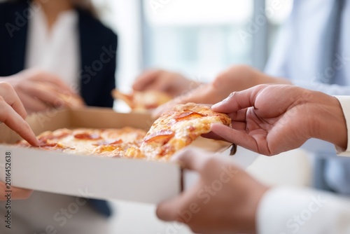 Office colleagues sharing a pepperoni pizza from a box during a lunch break. Close-up of hands taking a slice. Teamwork and corporate camaraderie concept