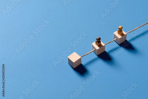 Wooden blocks with figures connected by a rope symbolizing a process. Business concept for teamwork, hierarchy, and supply chain structure on a blue background