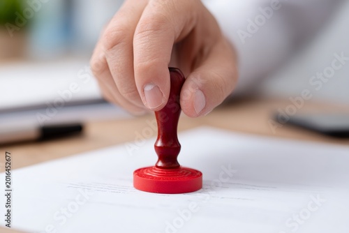 Close-up of a hand using a red stamp on an official document. Business concept of approval, authorization, and signing a contract