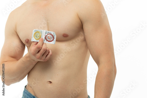 Slika na platnu A young guy with an athletic figure and a prominent torso is holding a condom in his hands